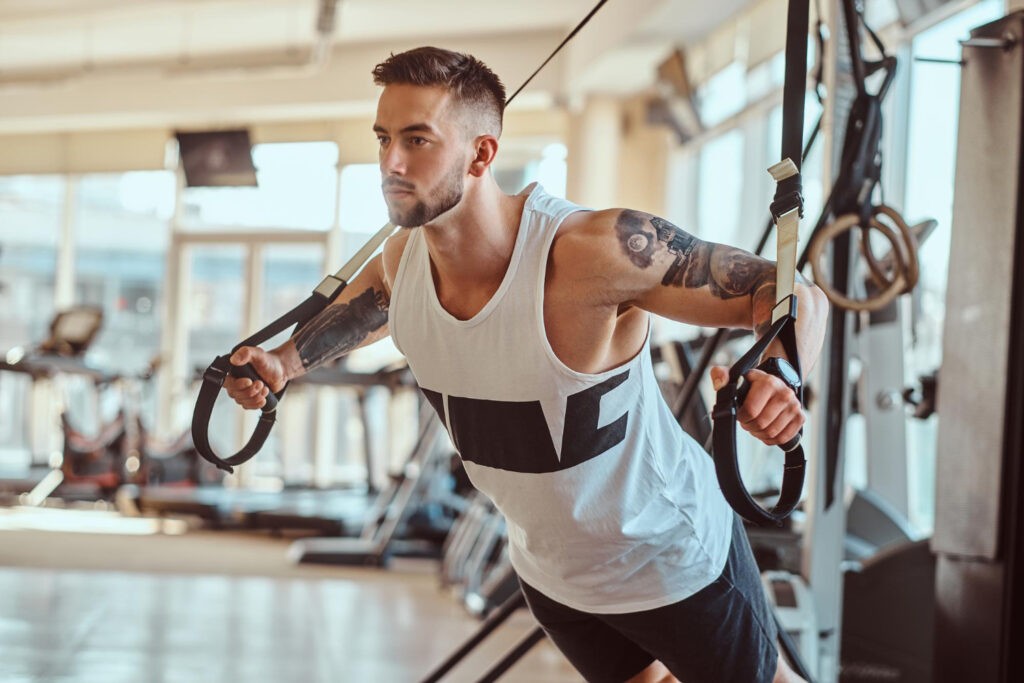 attractive-powerful-bodybuilder-is-doing-exercises-on-training-apparatus-at-sunny-gym